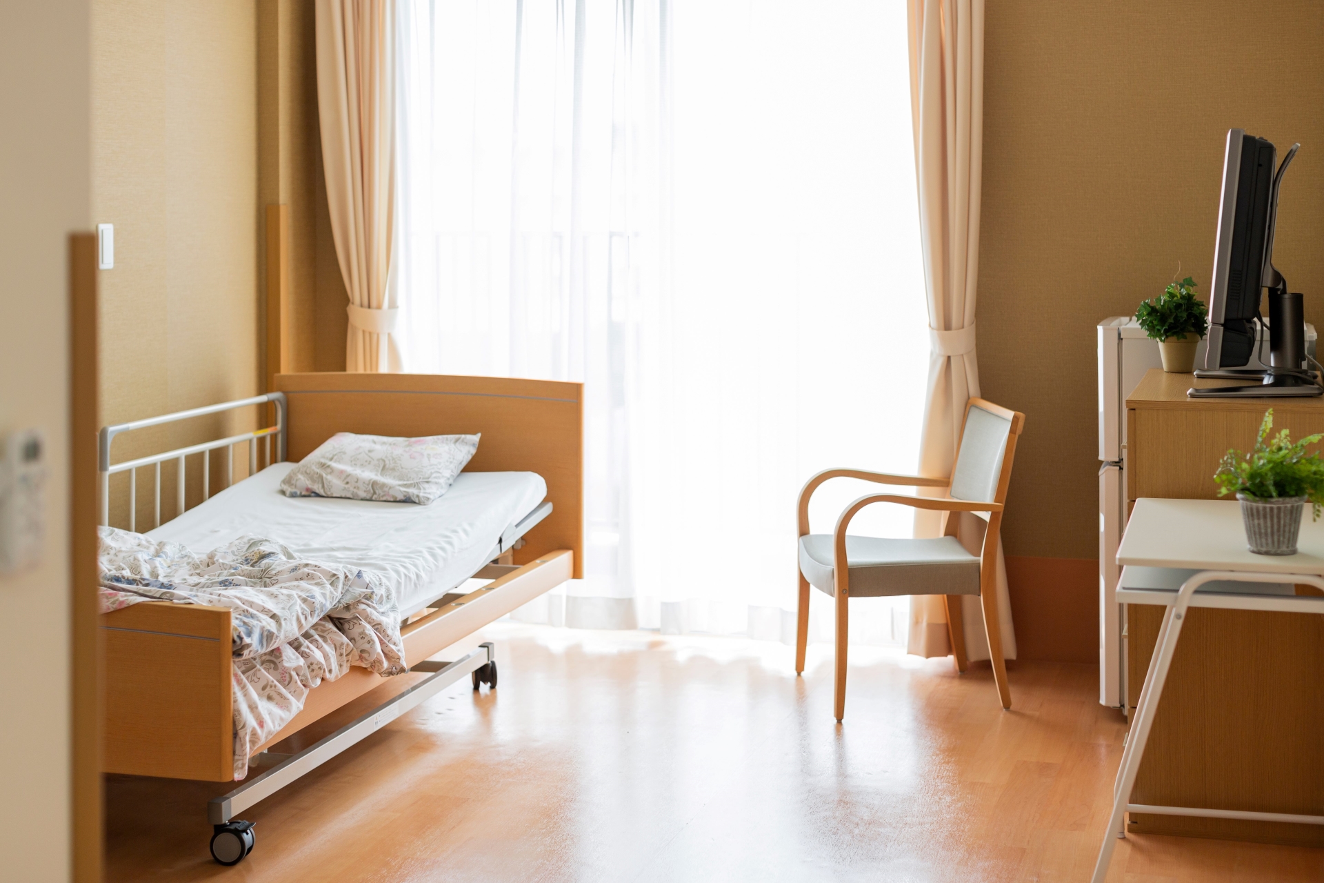 Insolvente Pflegeheimträger: Welche Verantwortung haben Pflegekassen?: Das Bild zeigt ein leeres Pflegezimmer. Auf der linken Seite steht ein benutztes Pflegebett. Auf der rechten Seite des Zimmers sind ein Stuhl sowie ein Tisch mit einem Fernseher zu sehen.
